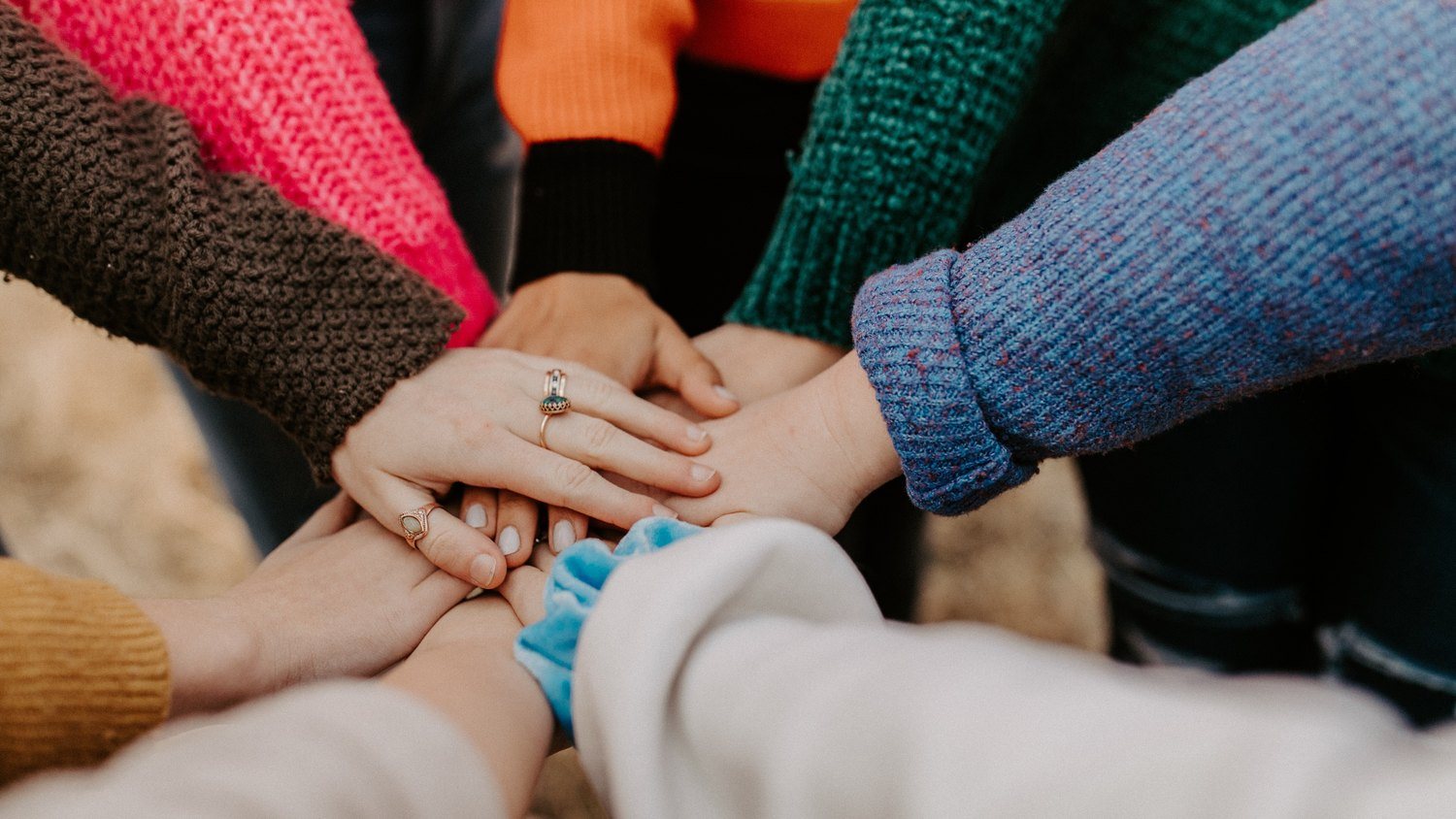 Several people's hands stacked one on top of another in the middle of a circle